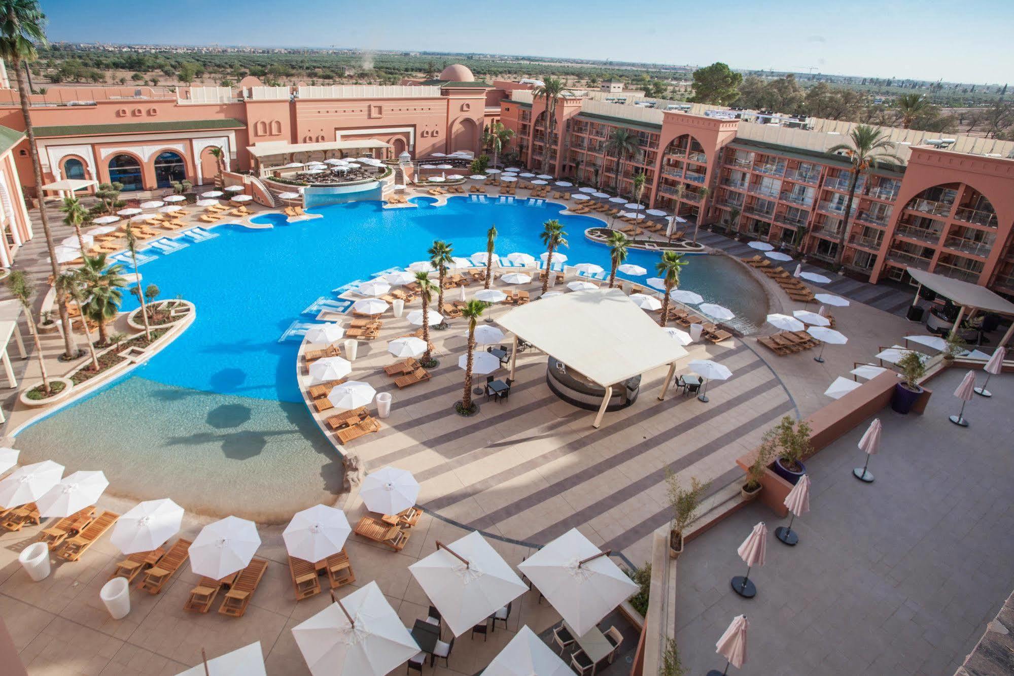 فندق سافوي لي جراند مراكش المظهر الخارجي الصورة The photo shows a large, luxurious hotel resort with a spacious swimming pool at its center. The pool area features several lounge chairs and umbrellas arranged around the water, providing a relaxing atmosphere for guests. Surrounding the pool are la